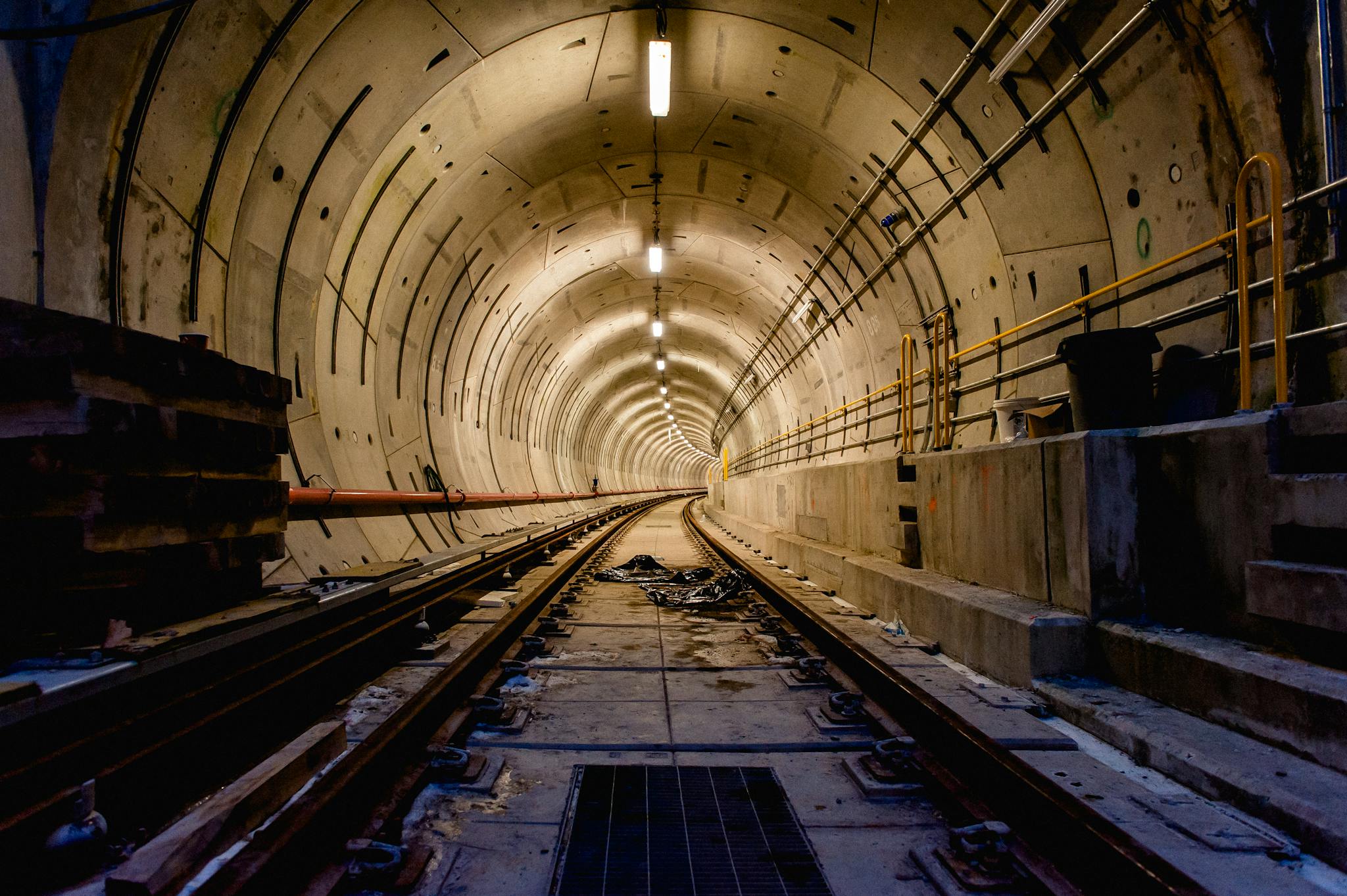 An empty underground tunnel with rail tracks illuminated by overhead lights.
